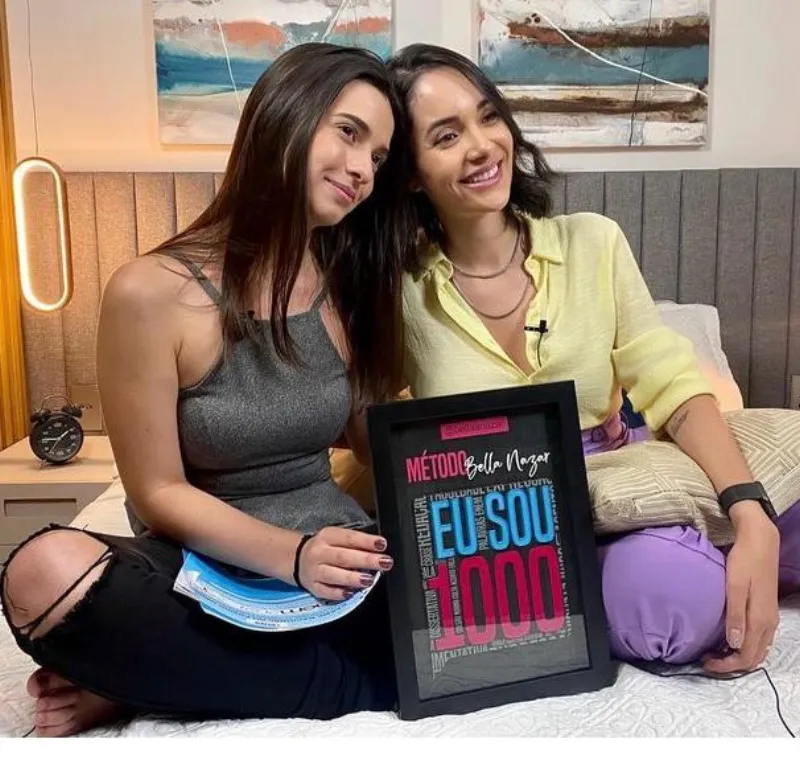 Bella Nazar sentada ao lado de aluna com o quadro 